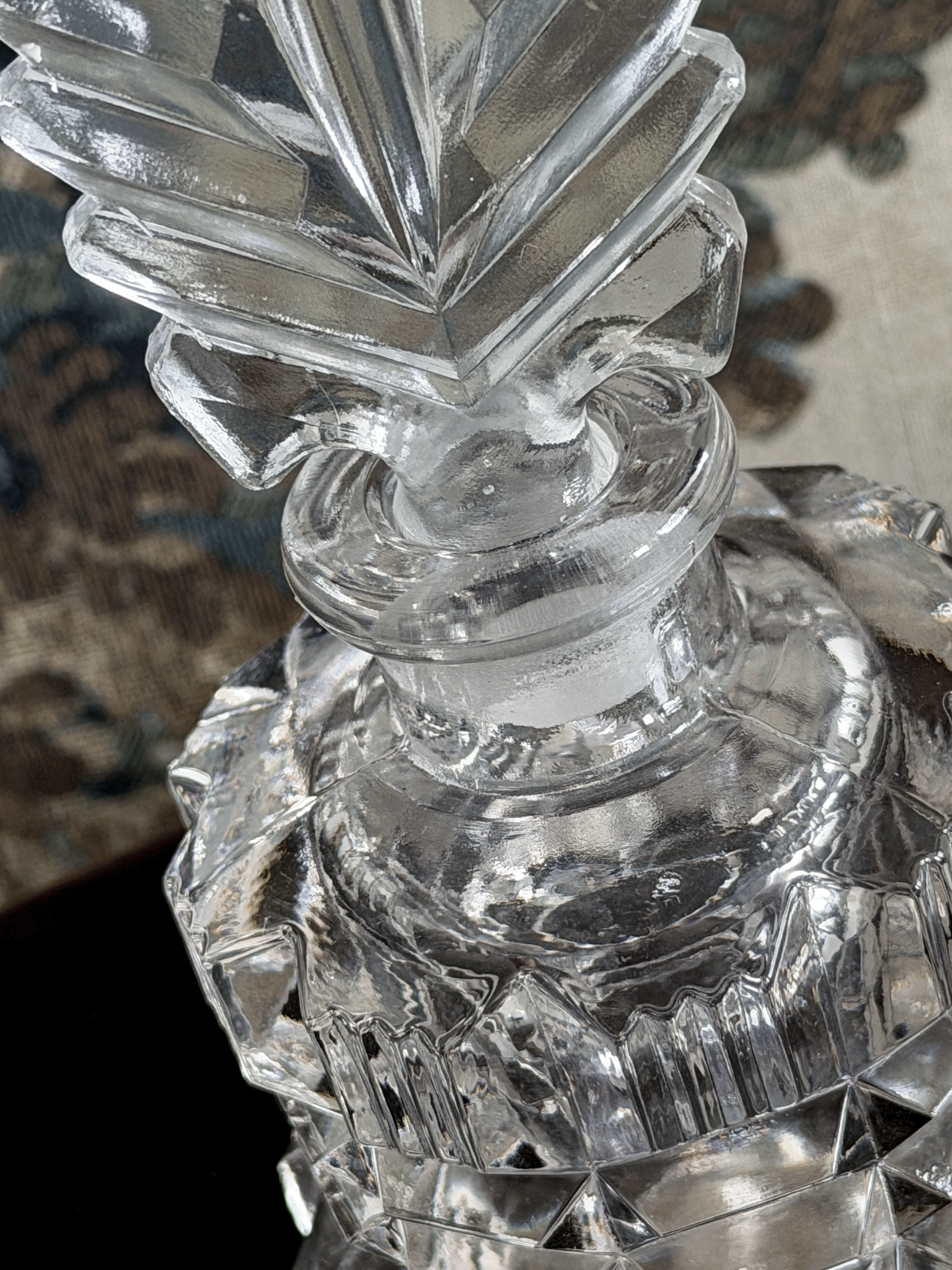 A close-up of a clear cut crystal perfume bottle with a faceted stopper.