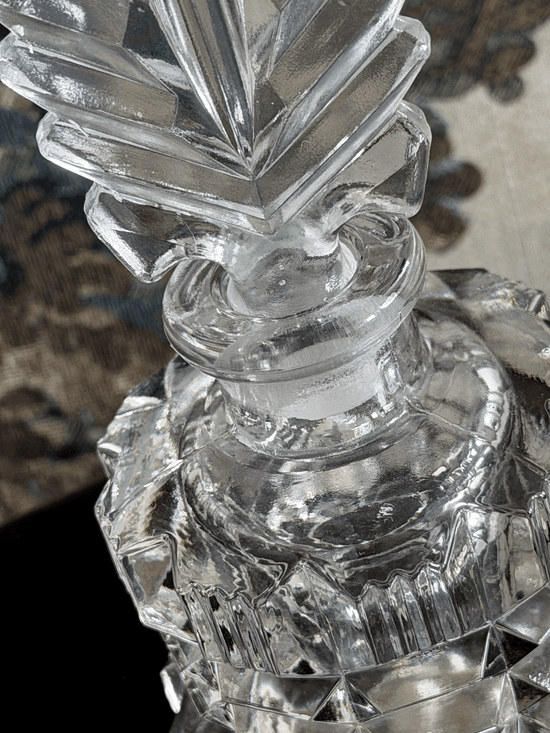 A close-up of a clear cut crystal perfume bottle with a faceted stopper.