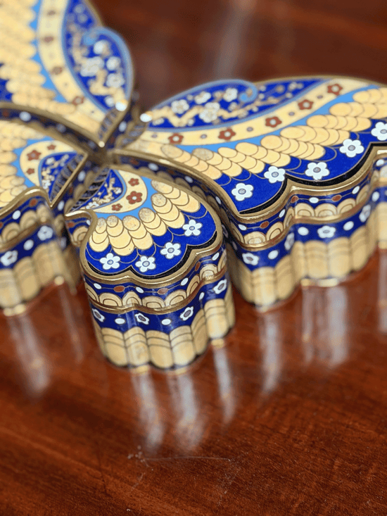 Decorative butterfly-shaped box with blue and gold patterns on a wooden surface