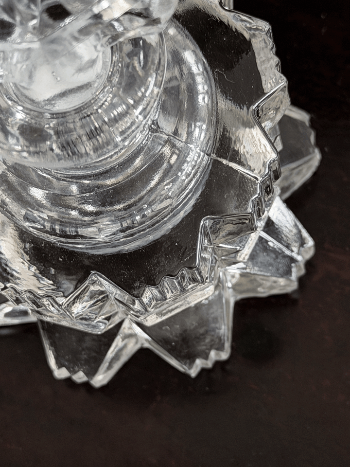A close-up of a clear cut-glass perfume bottle with faceted, geometric edges, resting on a dark brown surface.