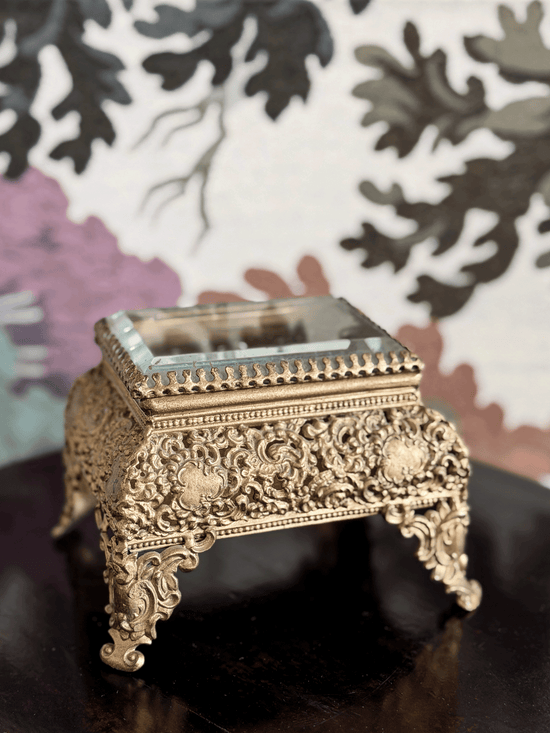 Vintage gold filigree jewelry box casket with raised ornate scroll feet and an attached hinged glass lid.