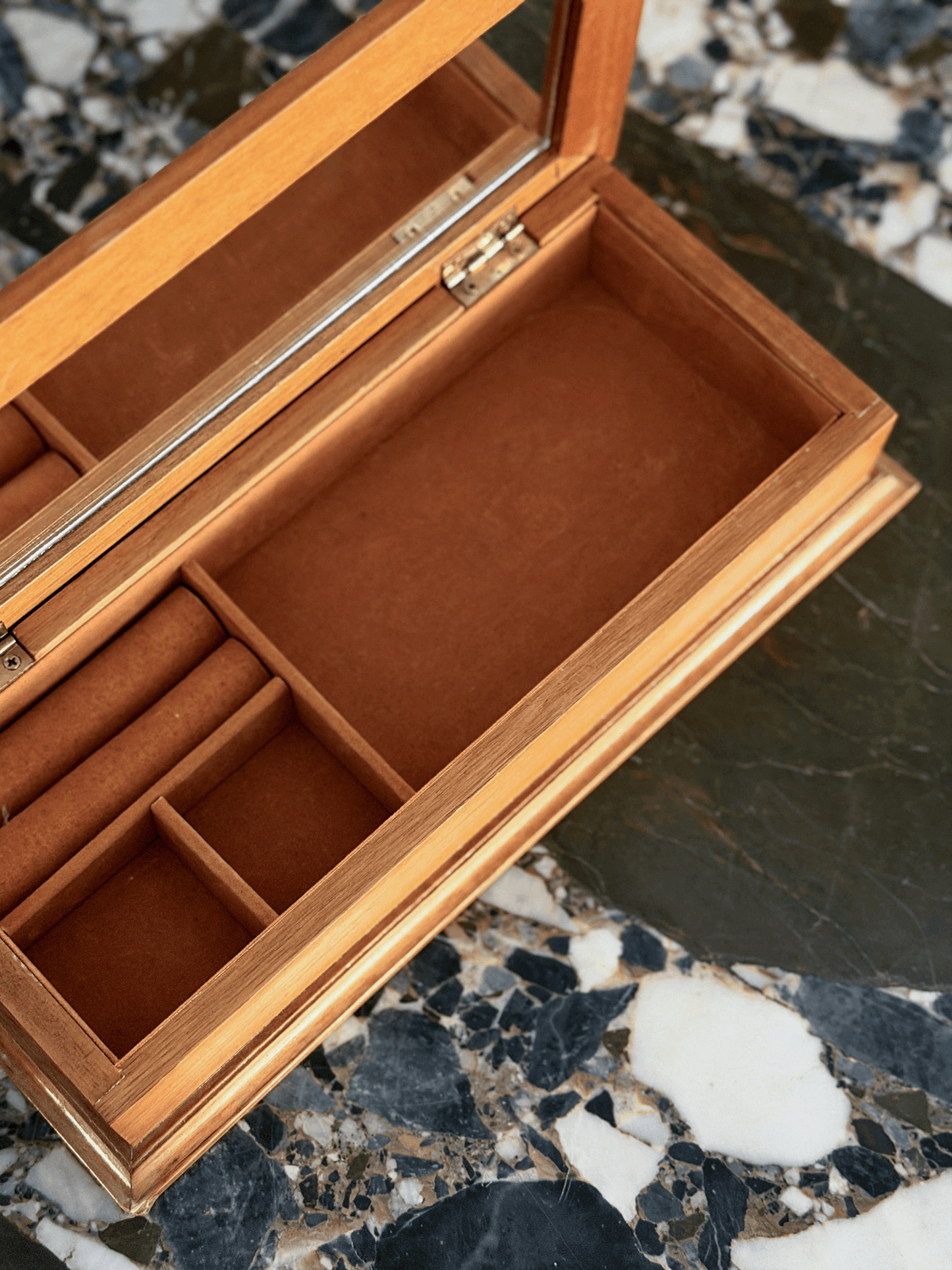 An open wooden jewelry box with a mirror on the lid, featuring a warm brown velvet interior with compartments and ring rolls.