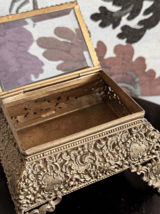 Open vintage gold filigree jewelry box casket with raised ornate scroll feet and an attached hinged glass lid.