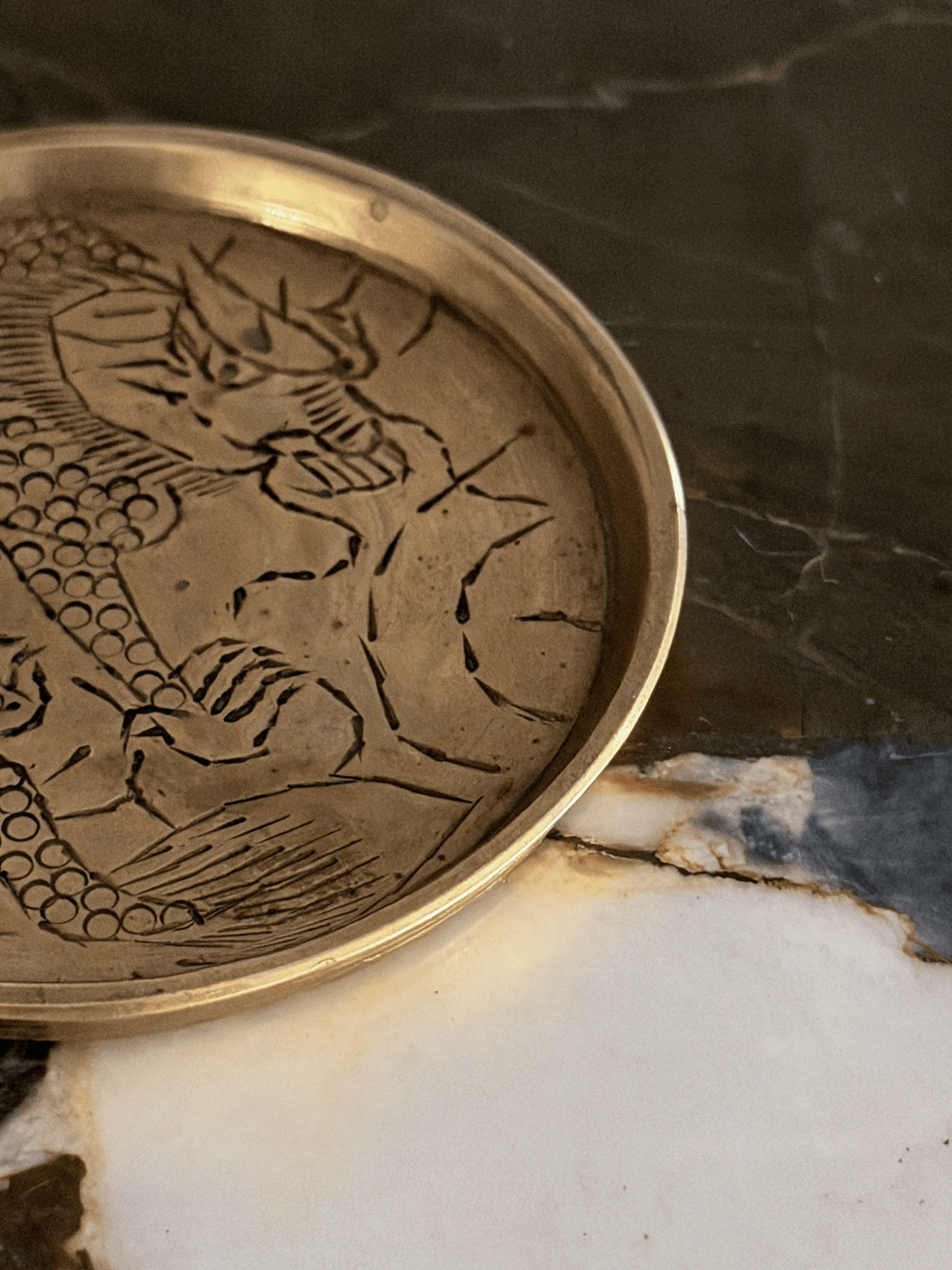 A close-up of a round metallic tray with an engraved dragon design, resting on a marble surface