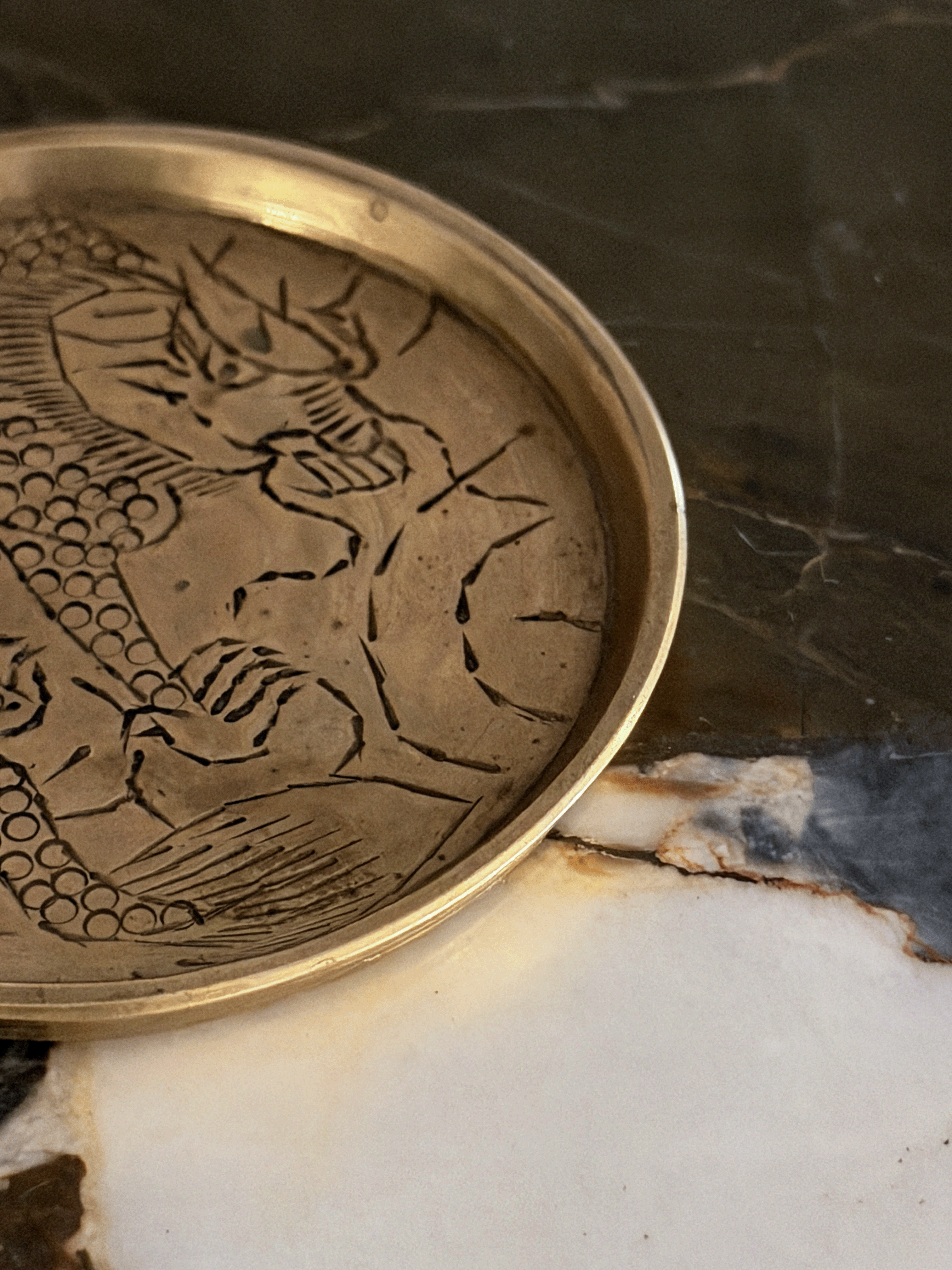 A close-up of a round metallic tray with an engraved dragon design, resting on a marble surface