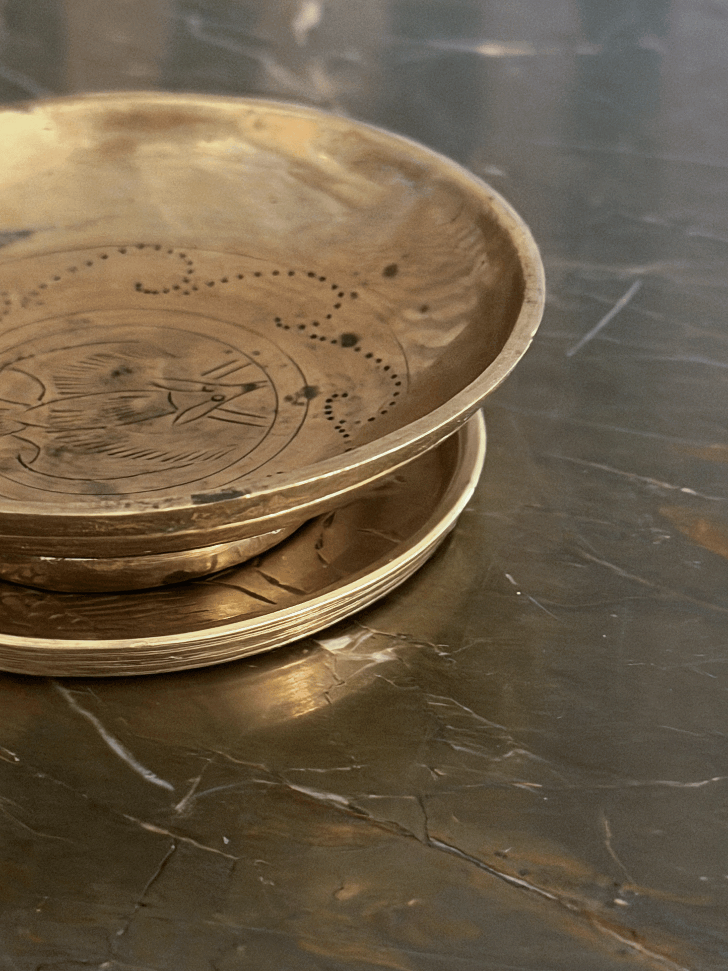 A stack of round brass plates with engraved patterns, resting on a dark, polished marble surface.