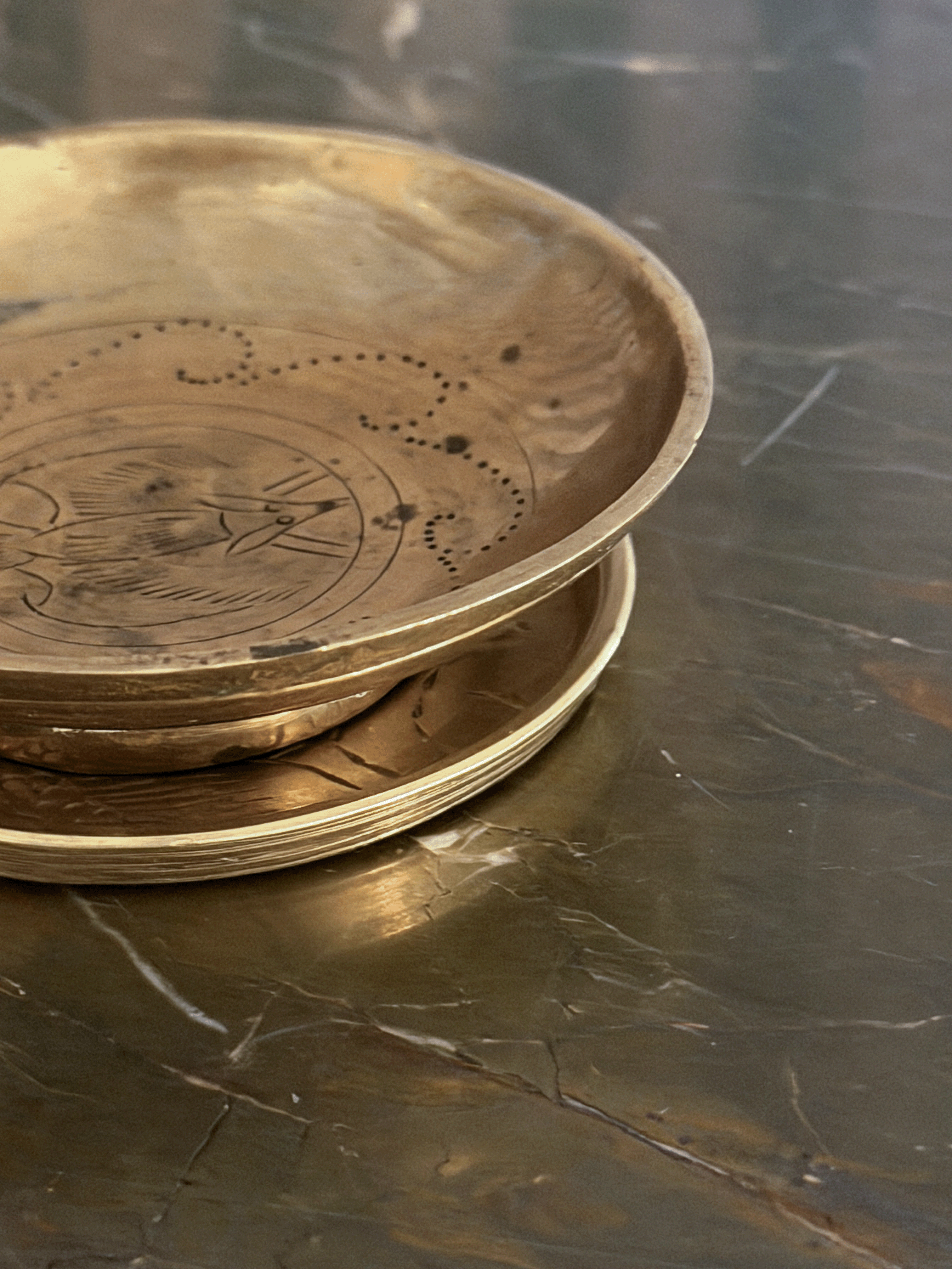 A stack of round brass plates with engraved patterns, resting on a dark, polished marble surface.