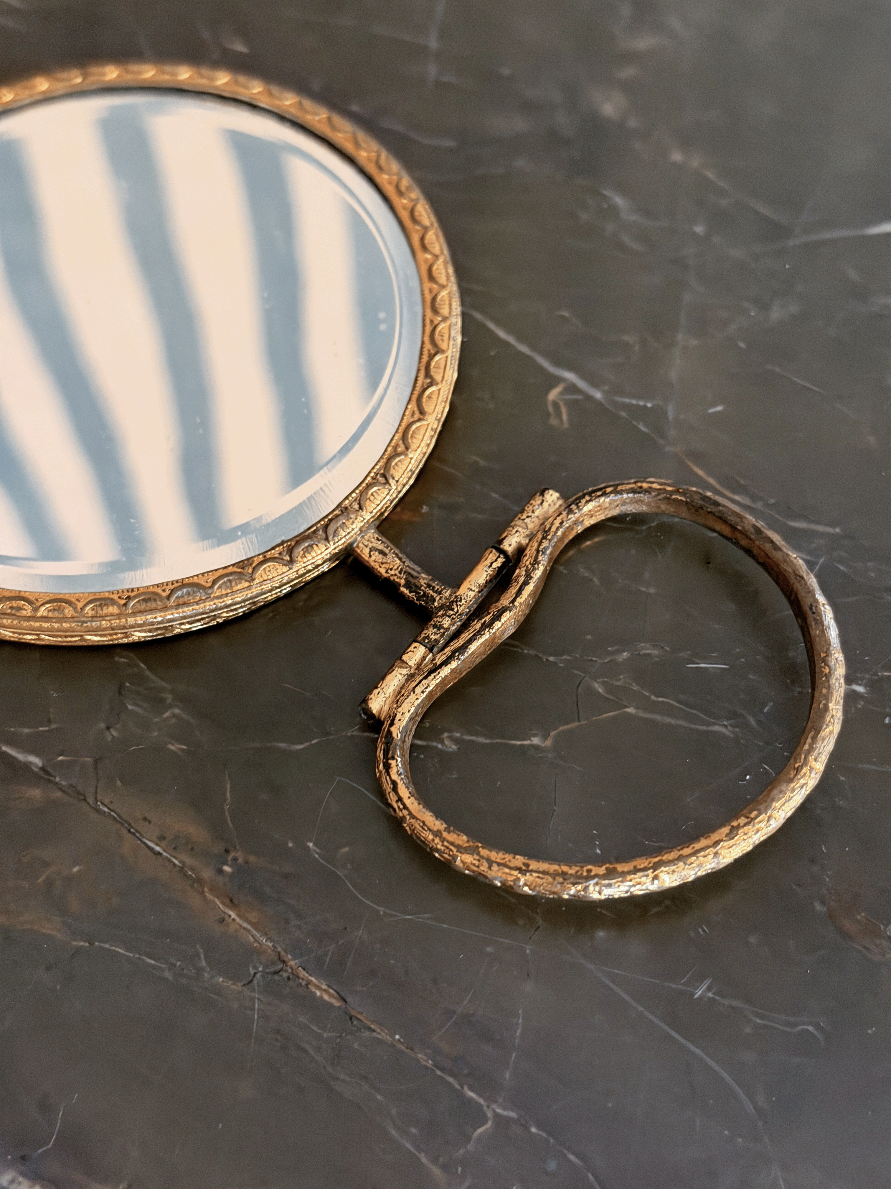 An antique-style oval hand mirror with a distressed gold frame and a matching ring pull handle