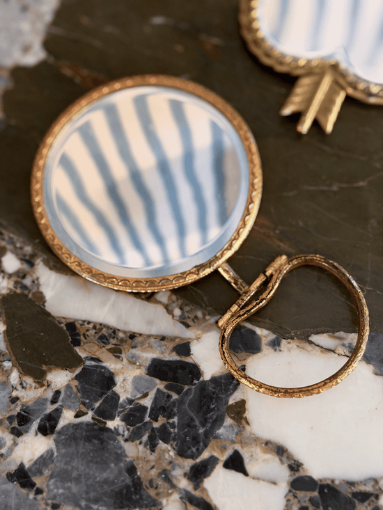A close-up of a round gold-tone handled vanity mirror with brass rope frame detailing